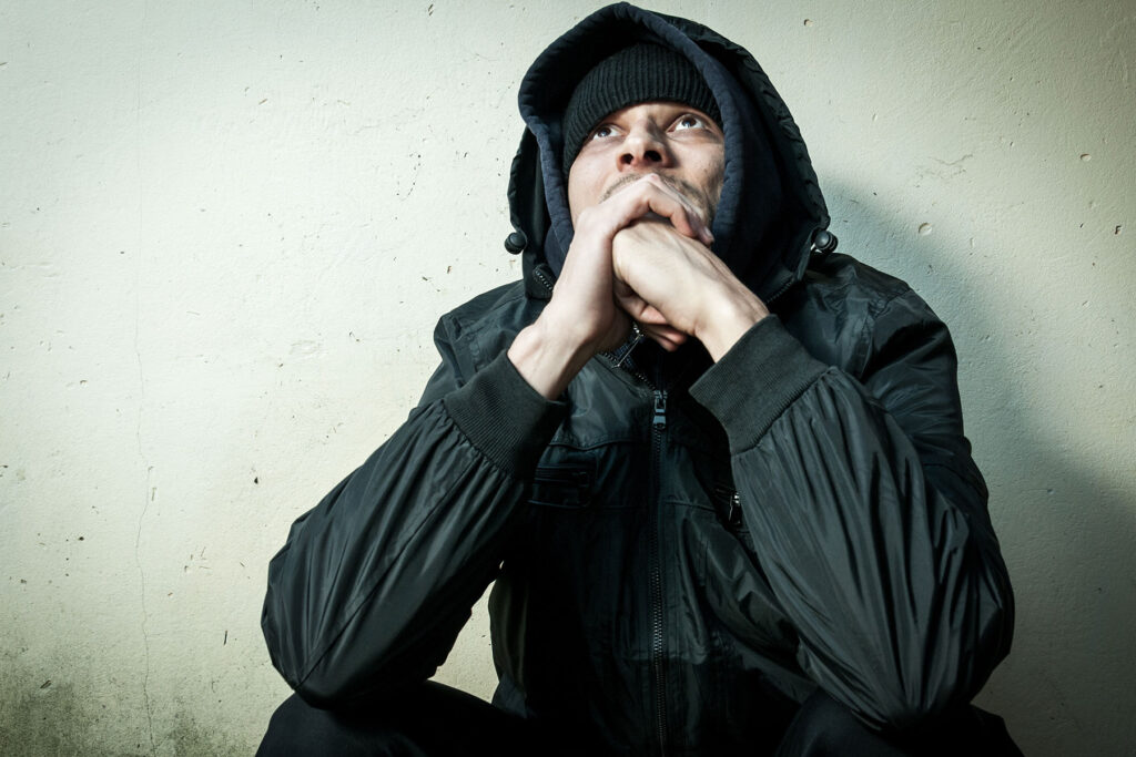 Man in hooded jacket sitting against a wall while experiencing heroin overdose symptoms