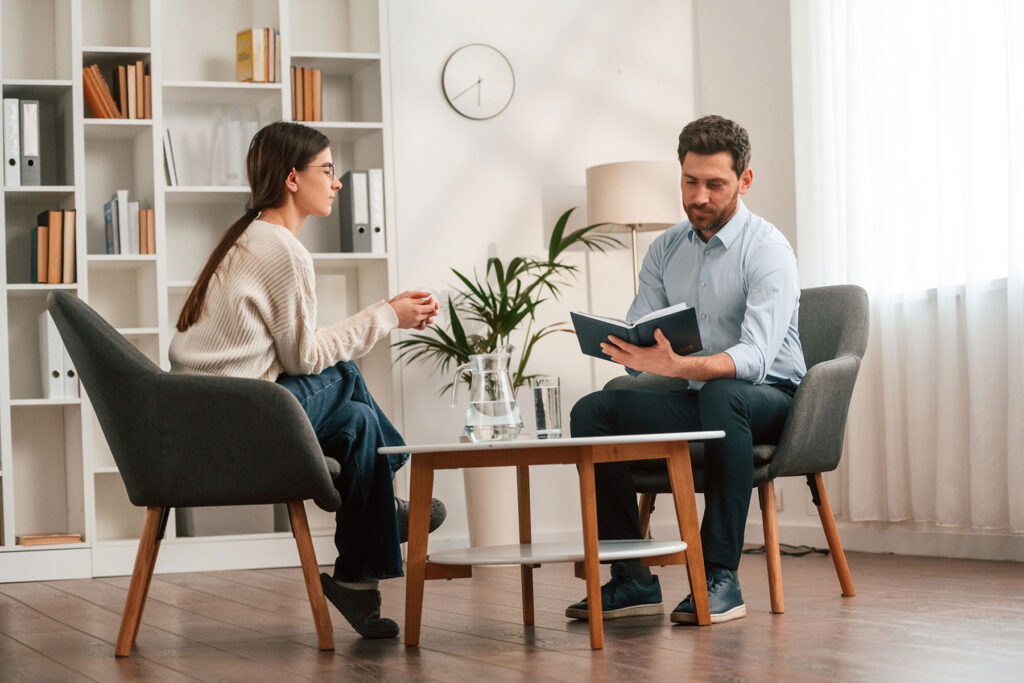 a woman sits with her therapist who is taking notes about their session and answers her question about is cbt effective for addiction