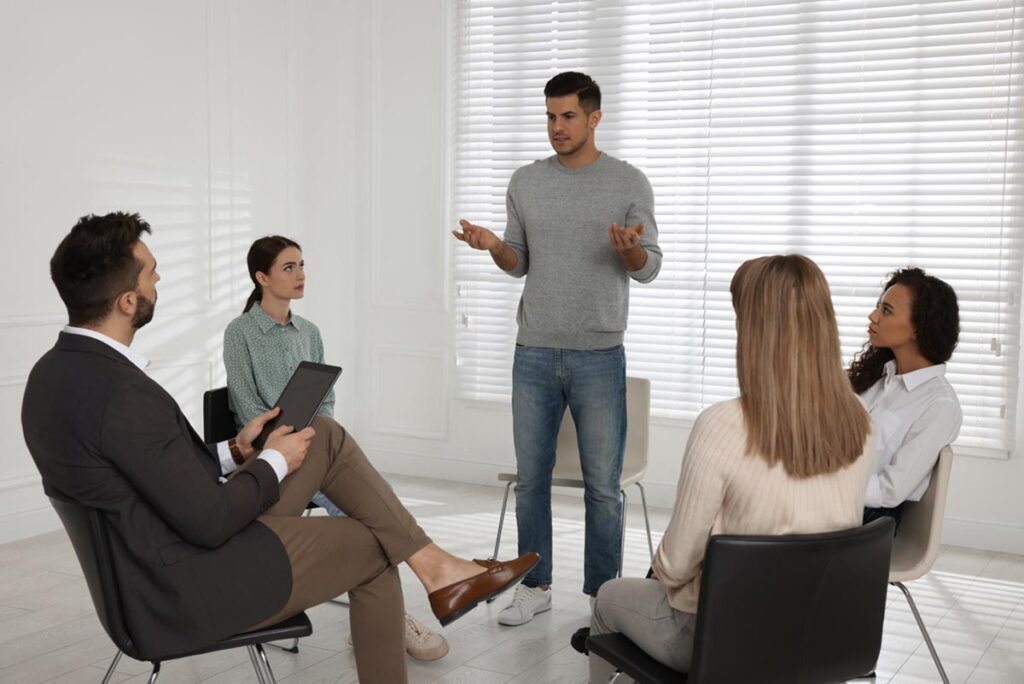 man standing up in circle of others in a heroin addiction treatment program