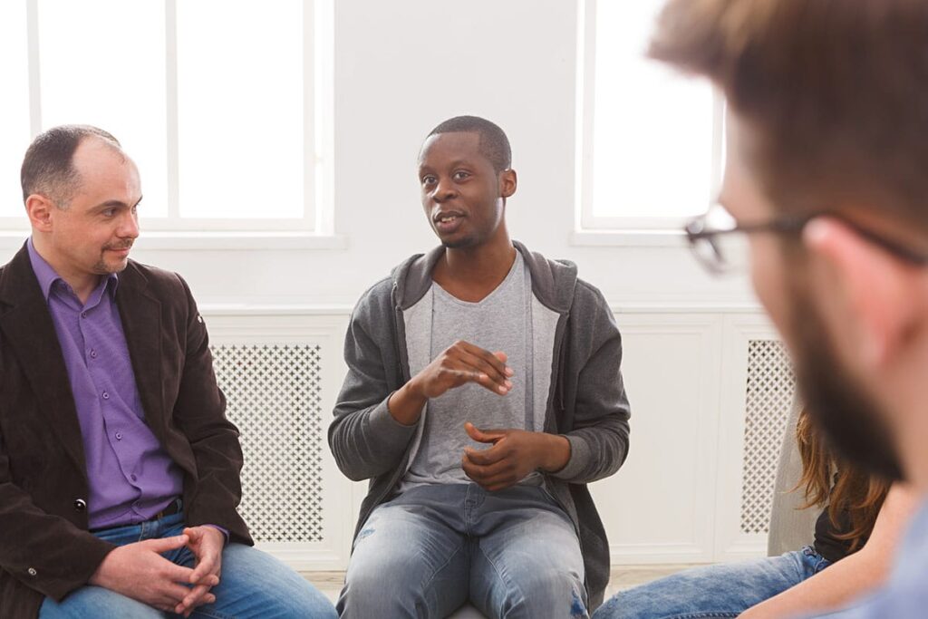 man in sweatshirt talks to peers in a men's rehab center